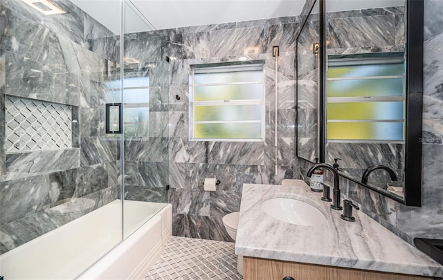 full bath with tile walls, toilet, vanity, and shower / bath combination with glass door