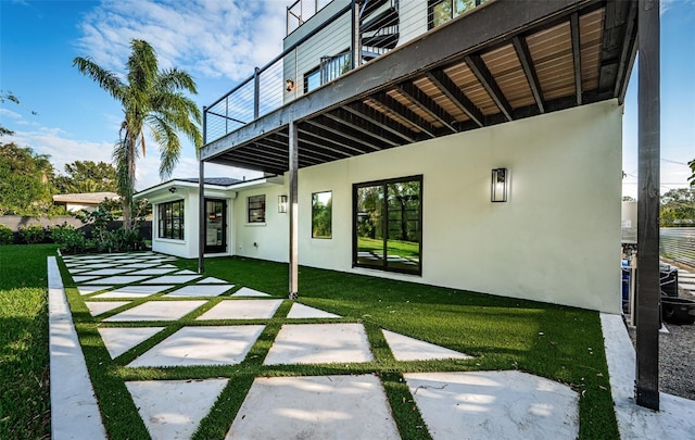 rear view of house with stucco siding, a patio area, and a lawn