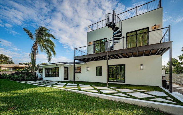 back of property with a balcony, stucco siding, and a lawn