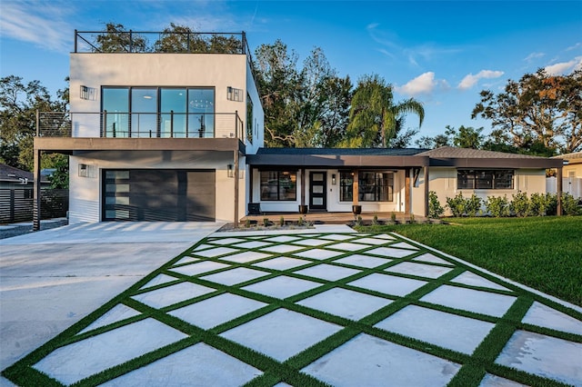 contemporary house featuring a porch, stucco siding, driveway, a garage, and a front yard