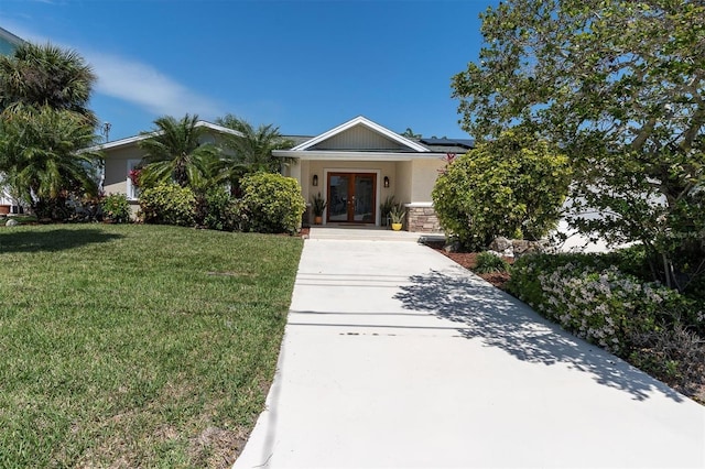 view of front facade featuring french doors, a front yard, solar panels, driveway, and stucco siding