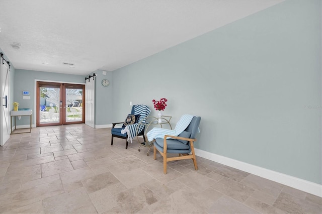 sitting room featuring baseboards, a barn door, stone tile flooring, and french doors