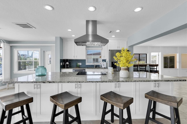 kitchen with wall chimney exhaust hood, black electric cooktop, decorative backsplash, white cabinets, and plenty of natural light
