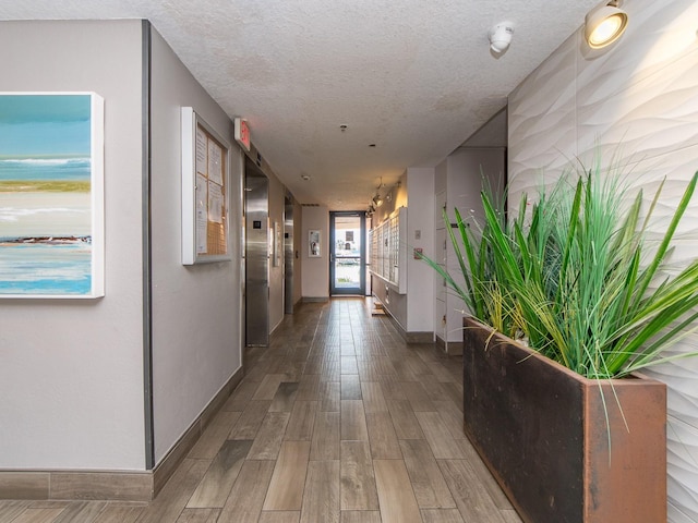 hallway with baseboards, a textured ceiling, wood finished floors, and elevator