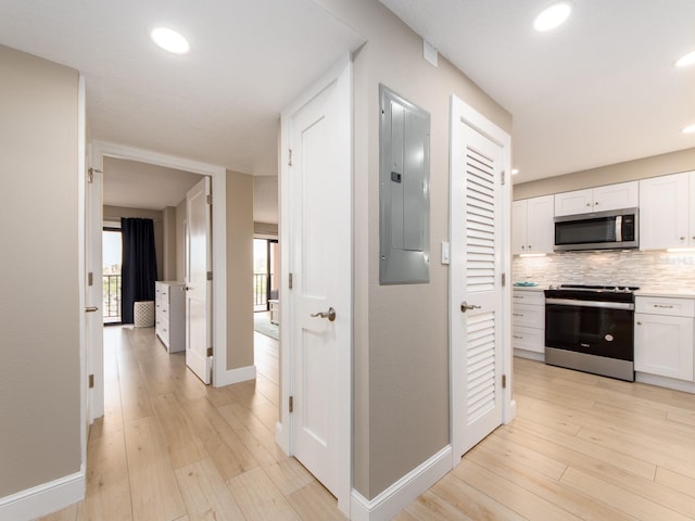 corridor with electric panel, baseboards, light wood-style flooring, and recessed lighting