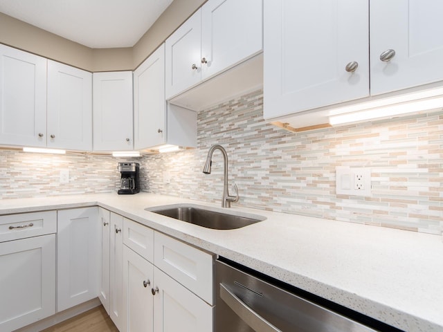 kitchen featuring stainless steel dishwasher, a sink, white cabinets, tasteful backsplash, and light stone countertops