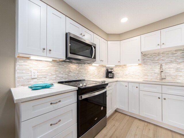 kitchen featuring appliances with stainless steel finishes, a sink, light wood-style floors, white cabinets, and recessed lighting