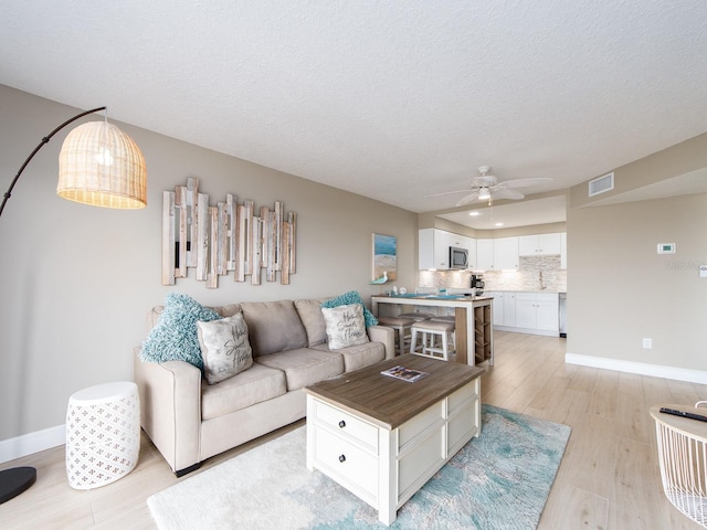 living area featuring a ceiling fan, light wood finished floors, baseboards, and a textured ceiling