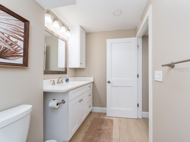 bathroom with wood finished floors, vanity, toilet, and baseboards