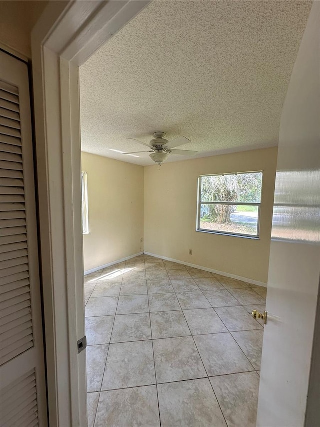 unfurnished room featuring light tile patterned flooring, ceiling fan, a textured ceiling, and baseboards