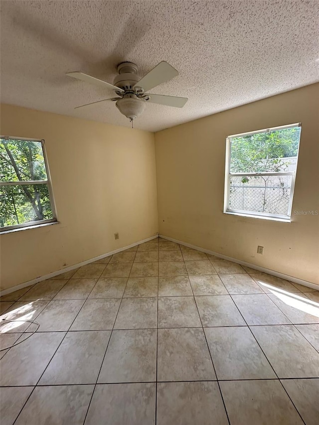 unfurnished room featuring healthy amount of natural light, light tile patterned floors, a textured ceiling, a ceiling fan, and baseboards
