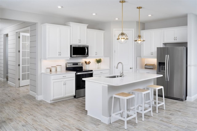 kitchen featuring appliances with stainless steel finishes, a sink, light countertops, light wood-style flooring, and a breakfast bar