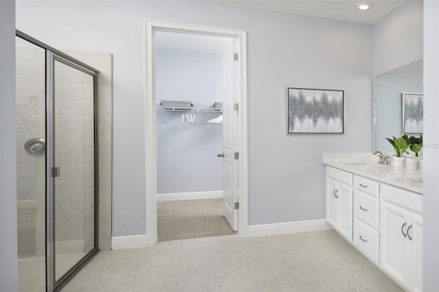 bathroom with a stall shower, a spacious closet, baseboards, double vanity, and recessed lighting