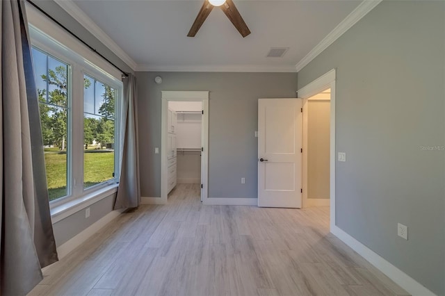 unfurnished bedroom featuring multiple windows, crown molding, light wood-style floors, a walk in closet, and baseboards