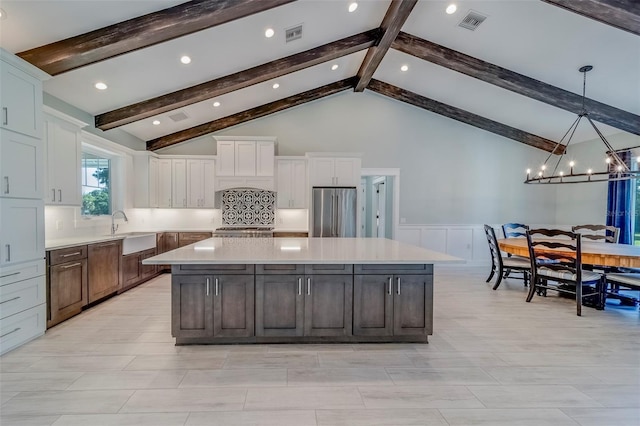 kitchen featuring freestanding refrigerator, a sink, a large island, wainscoting, and light countertops