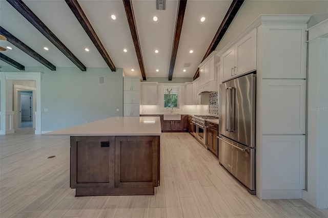 kitchen with high end appliances, beamed ceiling, white cabinetry, a center island, and light countertops