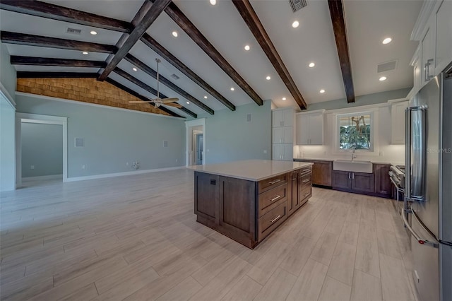 kitchen with stainless steel fridge, white cabinetry, a sink, light countertops, and a center island