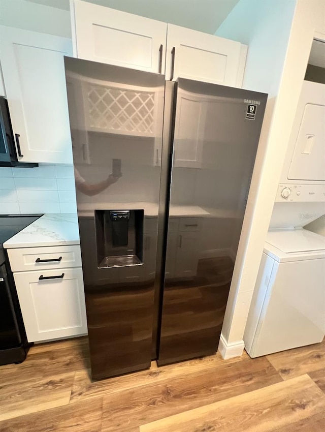 2424 W Tampa Bay Blvd Unit 203, Tampa, FL 33607 - kitchen with stainless steel fridge, stacked washer / dryer, light wood-style flooring, and white cabinetry