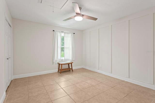 unfurnished bedroom with attic access, light tile patterned floors, a ceiling fan, and baseboards