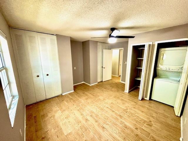 296 Lewfield Cir, Winter Park, FL 32792 - unfurnished bedroom featuring stacked washing machine and dryer, light wood-style flooring, a textured ceiling, multiple closets, and baseboards