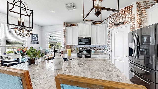 5040 Inshore Landing Dr, Apollo Beach, FL 33572 - kitchen featuring stainless steel appliances, a chandelier, white cabinetry, light stone counters, and tasteful backsplash