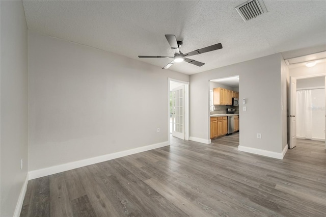 unfurnished living room featuring ceiling fan, wood finished floors, a textured ceiling, and baseboards