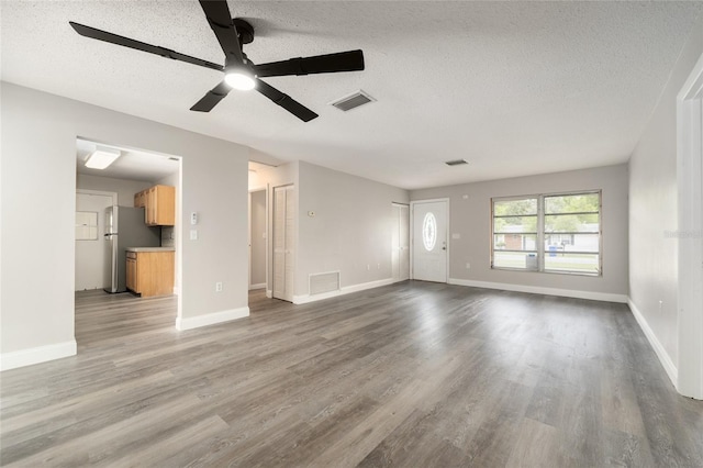 unfurnished living room with a textured ceiling, wood finished floors, a ceiling fan, and baseboards