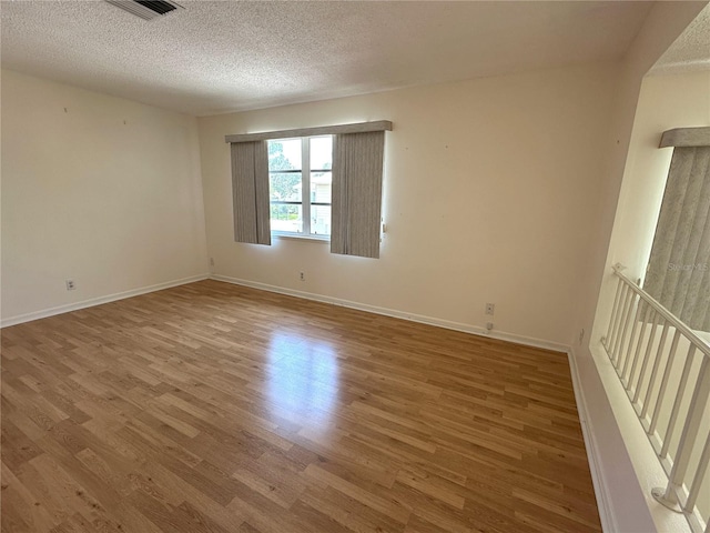 empty room featuring wood finished floors, a textured ceiling, and baseboards