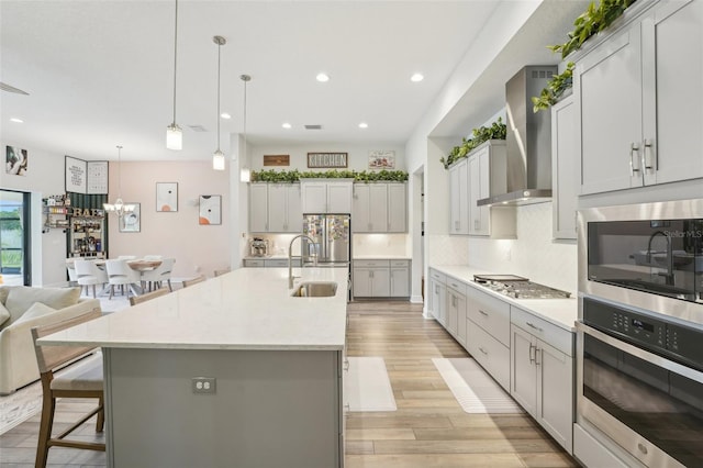 kitchen with stainless steel appliances, a sink, wall chimney range hood, tasteful backsplash, and a kitchen bar
