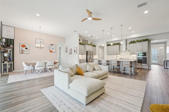 living area featuring light wood finished floors, ceiling fan, a chandelier, and recessed lighting