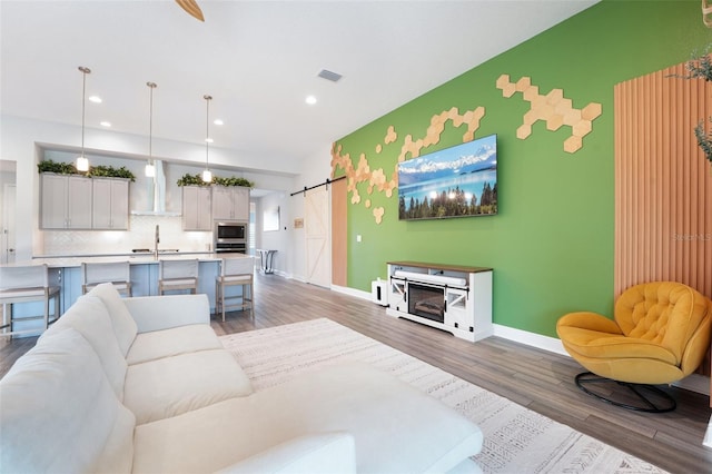 living area with a barn door, wood finished floors, baseboards, recessed lighting, and an accent wall