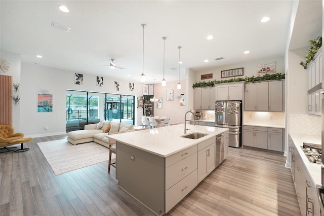 kitchen with stainless steel appliances, a sink, light wood-type flooring, open floor plan, and gray cabinetry