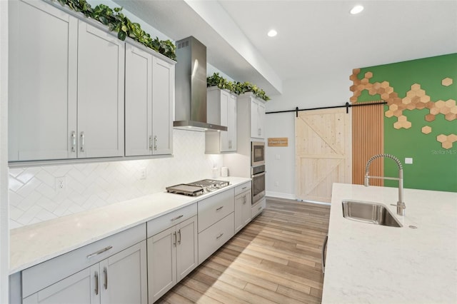 kitchen featuring wall chimney range hood, stainless steel gas stovetop, a sink, tasteful backsplash, and light wood-style floors