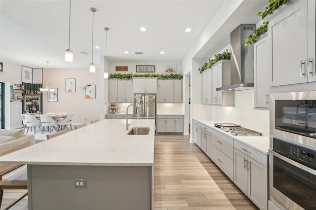 kitchen featuring wall chimney range hood, stainless steel appliances, a sink, tasteful backsplash, and a breakfast bar area
