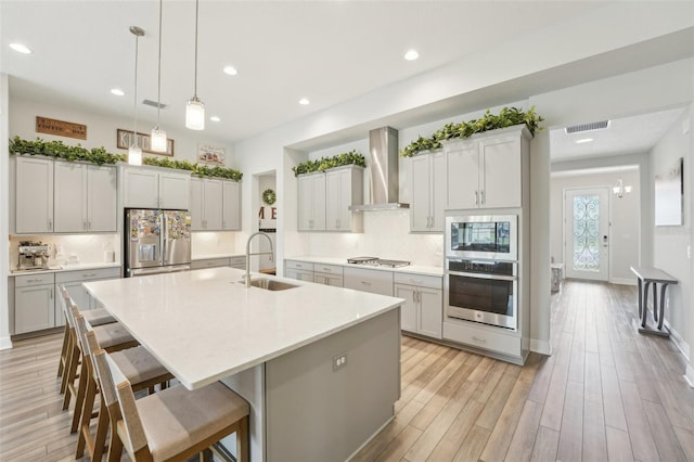 kitchen with appliances with stainless steel finishes, a sink, wall chimney range hood, recessed lighting, and an island with sink