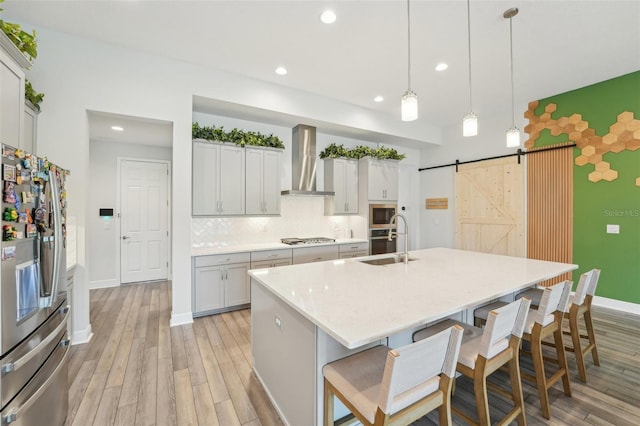 kitchen featuring stainless steel appliances, wall chimney range hood, a barn door, a sink, and light wood-style floors