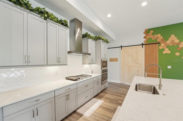 kitchen featuring wall chimney range hood, a sink, stainless steel appliances, light countertops, and recessed lighting