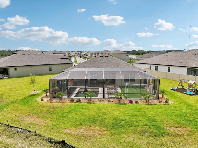back of property with a yard, a pool, a residential view, and glass enclosure