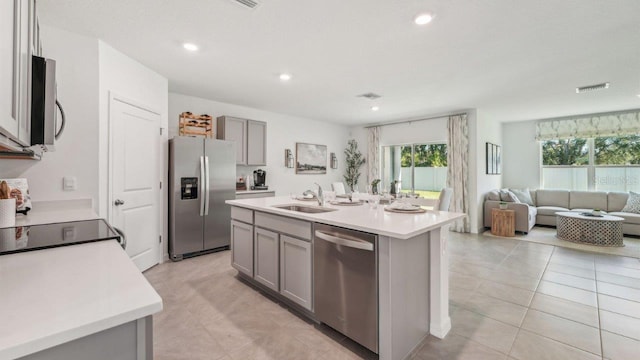 kitchen featuring appliances with stainless steel finishes, gray cabinetry, a sink, open floor plan, and light countertops