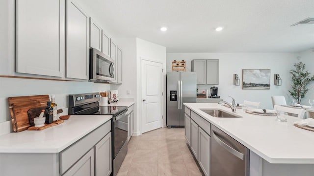 kitchen featuring stainless steel appliances, a sink, gray cabinets, a kitchen island with sink, and light countertops