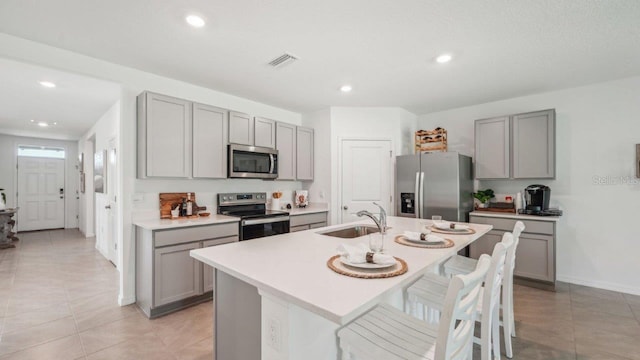 kitchen with stainless steel appliances, gray cabinets, a sink, recessed lighting, and a breakfast bar area