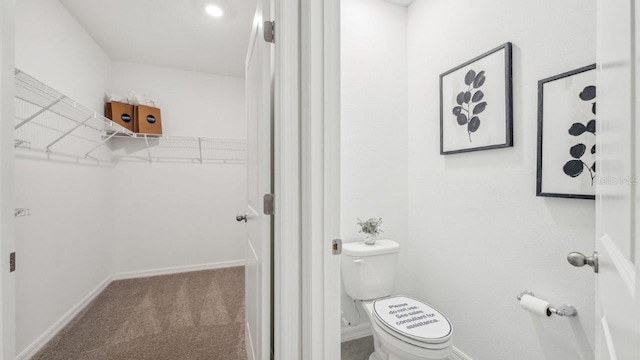 bathroom with toilet, a spacious closet, and baseboards
