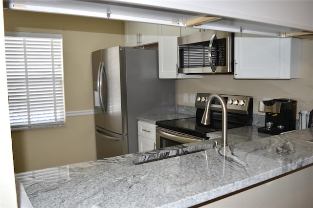 kitchen with appliances with stainless steel finishes, light stone counters, and white cabinetry