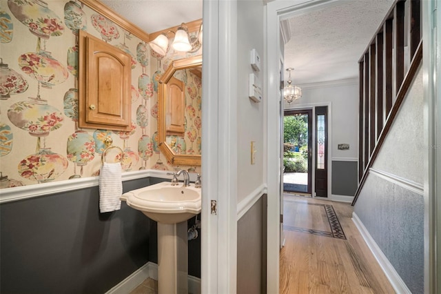 bathroom featuring baseboards, wood finished floors, ornamental molding, wallpapered walls, and a textured ceiling