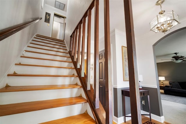 stairway featuring arched walkways, ornamental molding, a ceiling fan, and a chandelier