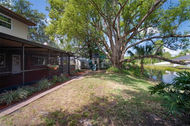 view of grassy yard with a sunroom and a water view