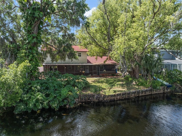rear view of property featuring a water view, a yard, roof with shingles, and a sunroom
