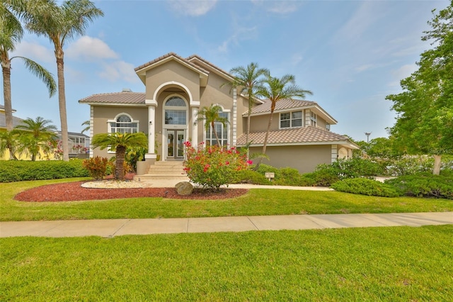 mediterranean / spanish-style house with stucco siding, a front yard, a tiled roof, and french doors