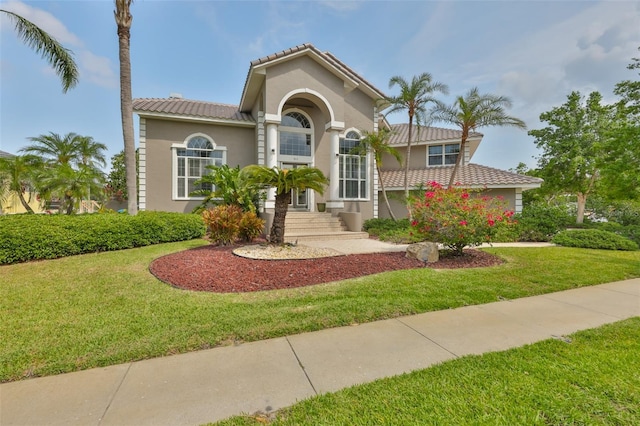 mediterranean / spanish-style house featuring stucco siding, a tile roof, and a front lawn