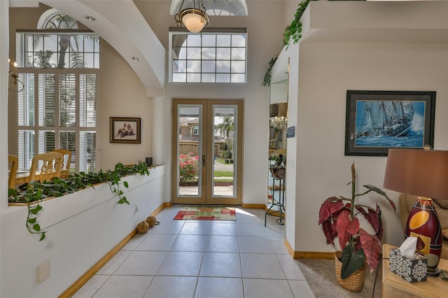 foyer entrance with french doors, arched walkways, baseboards, light tile patterned flooring, and a high ceiling